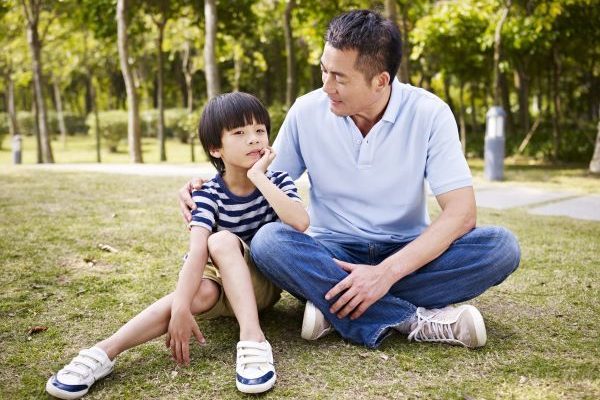 boy sitting on the grass with his smiling father