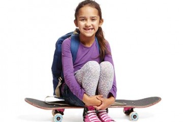Smiling young girl sitting on a skateboard wearing a backpack