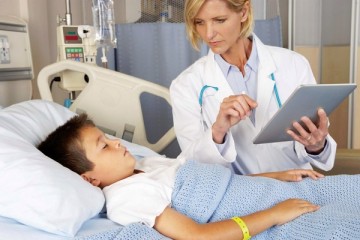 Physician with ipad at bedside of young boy