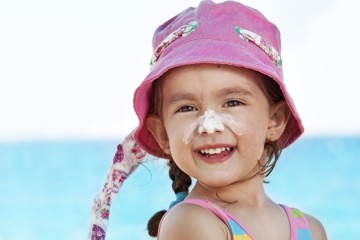 Smiling girl at the beach wearing pink hat and suncreen on her nose