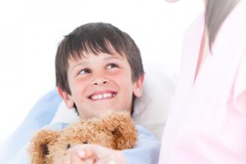 Smiling boy holding teddy bear with nurse at bedside