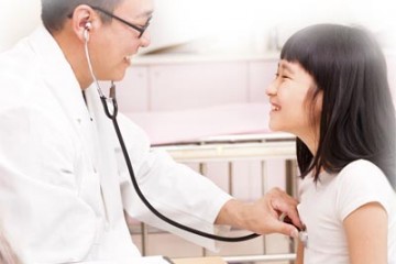 Girls smiles as physician listens to her heart