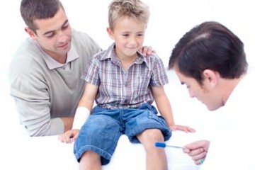 Father watches as physician gives young boy physical examination.
