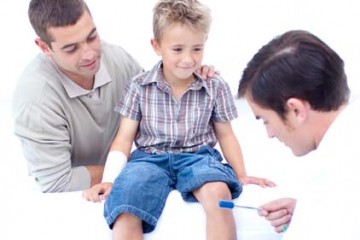 Father watches as physician gives young boy physical examination.