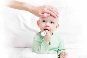 Hand on the forehead of toddler with thermometer