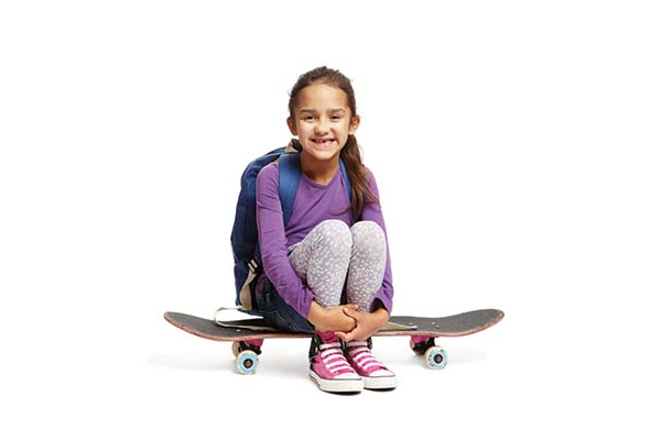 Smiling young girl sitting on a skateboard wearing a backpack