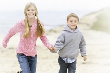 Sister and brother running and holding hands at the beach