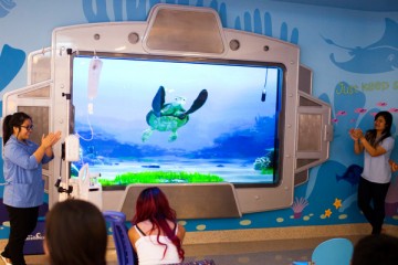 Patients watching Turtle Talk in CHOC lobby while volunteers help with the program