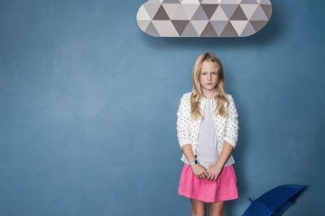 Sad girl standing under storm cloud next to umbrella on the floor