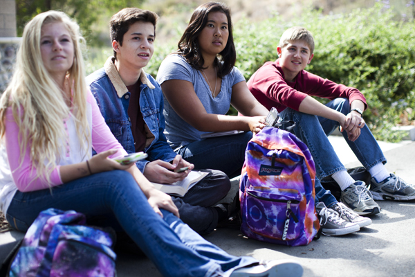 Teen boys and girl sitting on the ground with backpacks