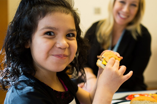 Young girl eating with clinical dietitian smiling in the background