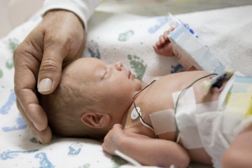 father touching head of premature infant NICU