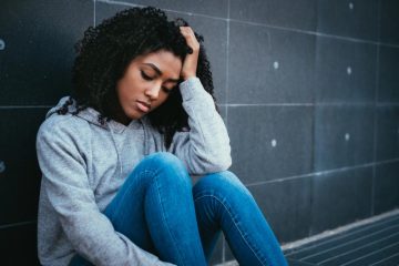 Teenage girl sits against wall looking stressed