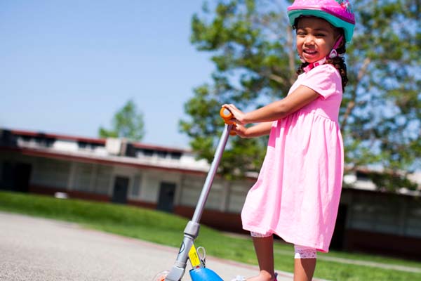 Young girl on a scooter in pink dress wearing a helmet
