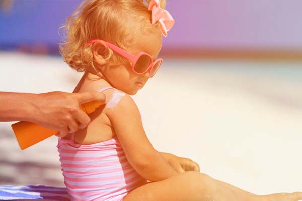 Mom applying sunscreen on toddler with sunglasses at the beach