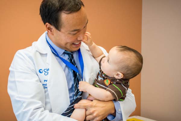 Pediatric surgeon smiling and holding infant boy