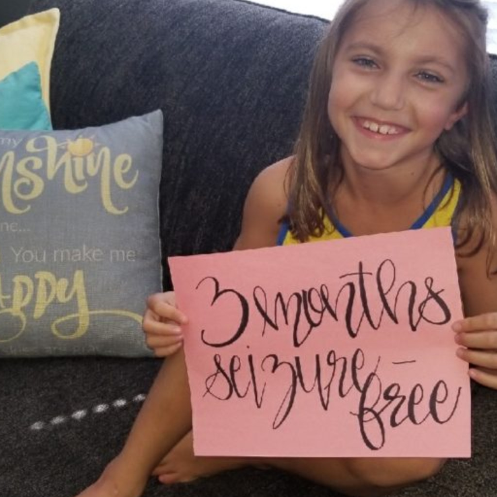 Smiling Rylee holding three months seizure free sign