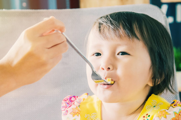 Young girl being fed with fork by parent