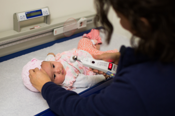 baby girl wearing pink hat having temperature taken with thermometer by nurse at clinic on scale