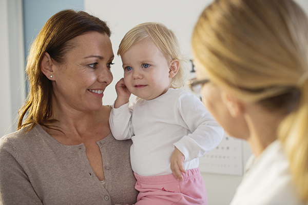 Toddler girl pulling on ear with mom and pediatrician