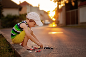 Little boy wearing hat playing with toy cars in the road