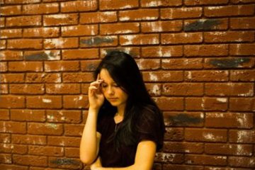 Troubled teen girl standing by a brick wall