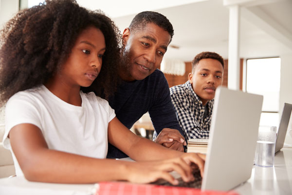 teen girl on computer with dad and brother over shoulder