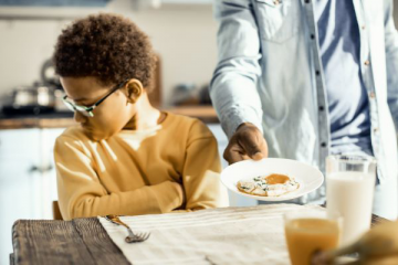 young boy refusing a plate of food from his father