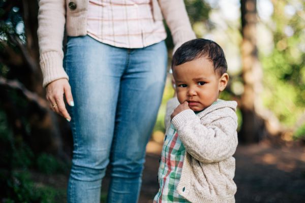 toddler with hand in his mouth standing next to mom