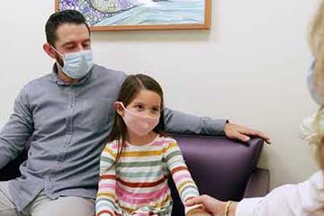 father and daughter with masks talking to physician