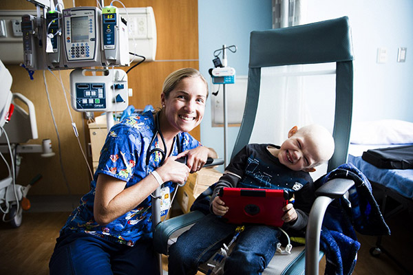 Female oncology nurse sits with smiling young male patient