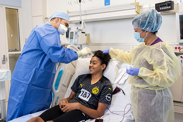 A teenage boy smiles as he receives a Brineura infusion from neurosurgeon Dr. Joffre Olaya