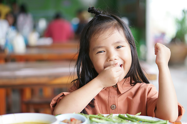 Young girl eats asparagus at a school table