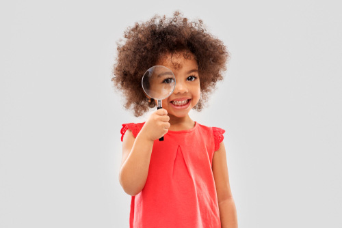 Young girl smiles and looks through magnifying glass