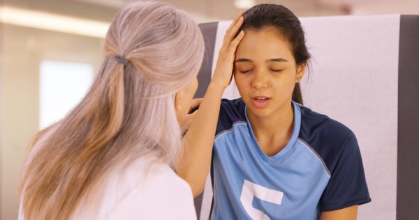 Young female athlete holds head and winces during doctor visit