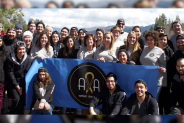 A group of CHOC patients and staff holding a blue AYA banner in the mountains.