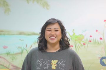 A woman in a grey Choco long sleeve t-shirt standing in front of an art mural.