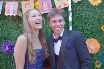 Two attendees of the CHOC Oncology Patient Ball is a dress and tuxedo in front of a decorative floral background.